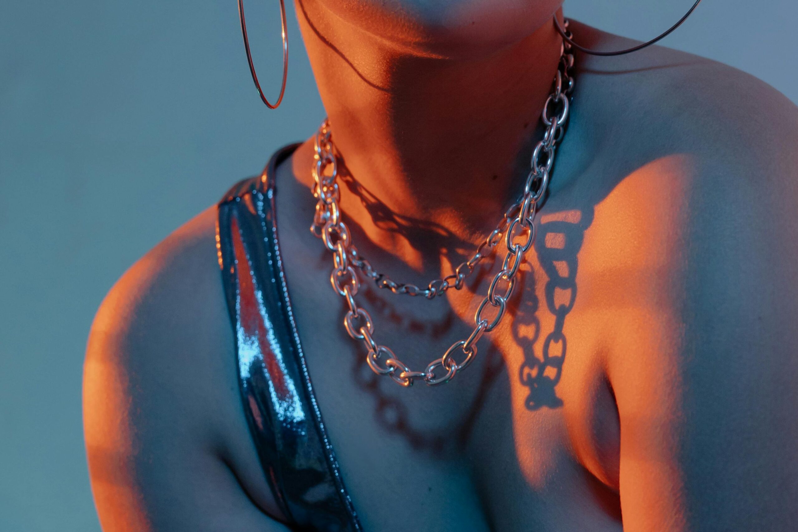 Close-up of a person wearing a shiny outfit with a chain necklace, illuminated by dramatic lighting.